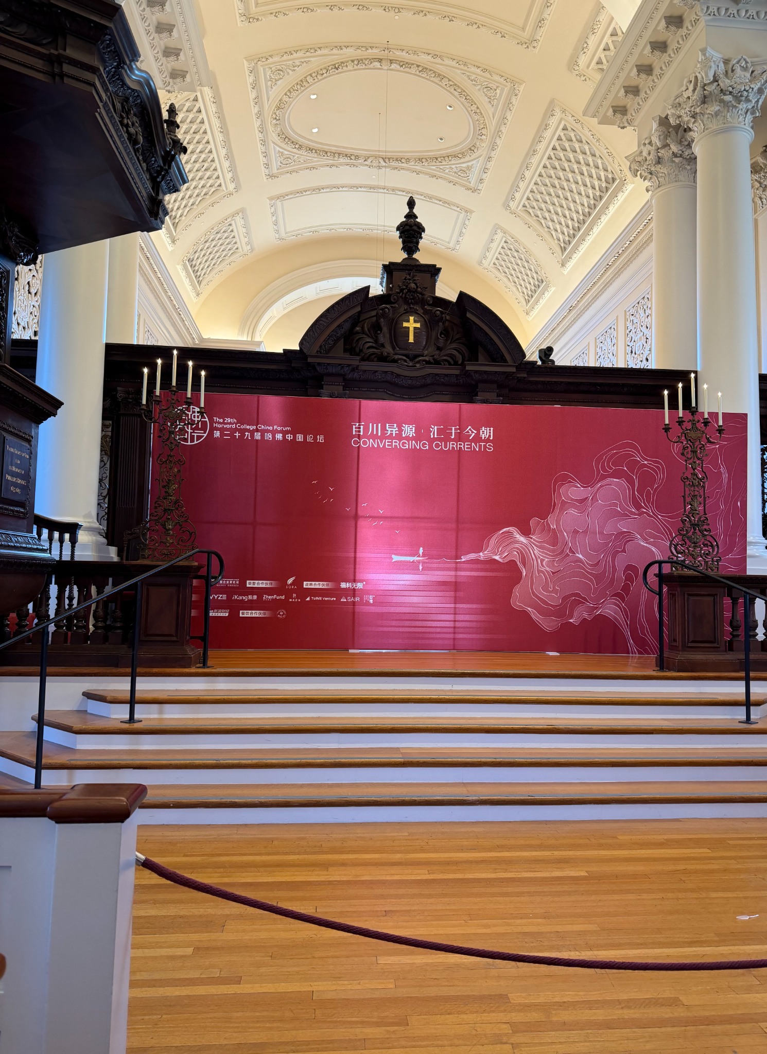 Red Converging Currents backdrop at Harvard College China Forum, framed by an ornate vaulted ceiling and broad stage steps.