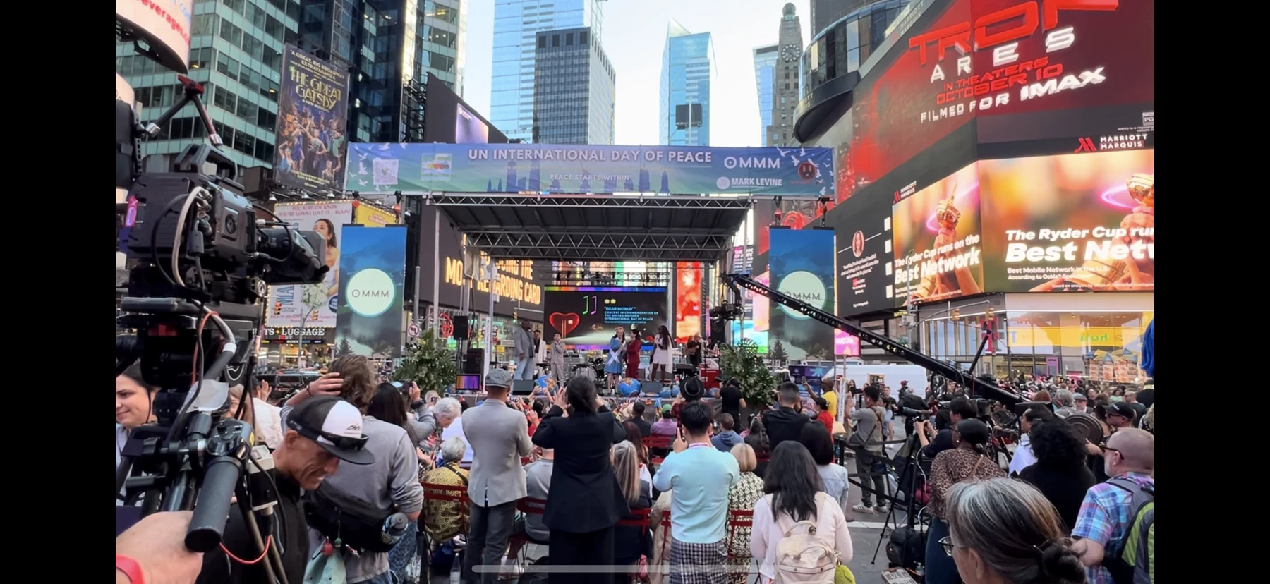 Audience and public stage in Times Square beneath the UN International Day of Peace and OMMM event banner.