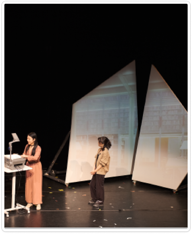 Performers on a theatre stage framed by a geometric set.